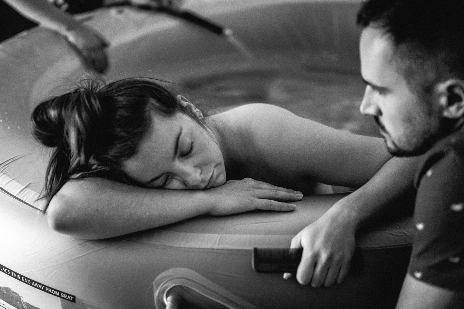 Black and white intimate photograph showing couple sharing a tender moment while resting against a guitar.
