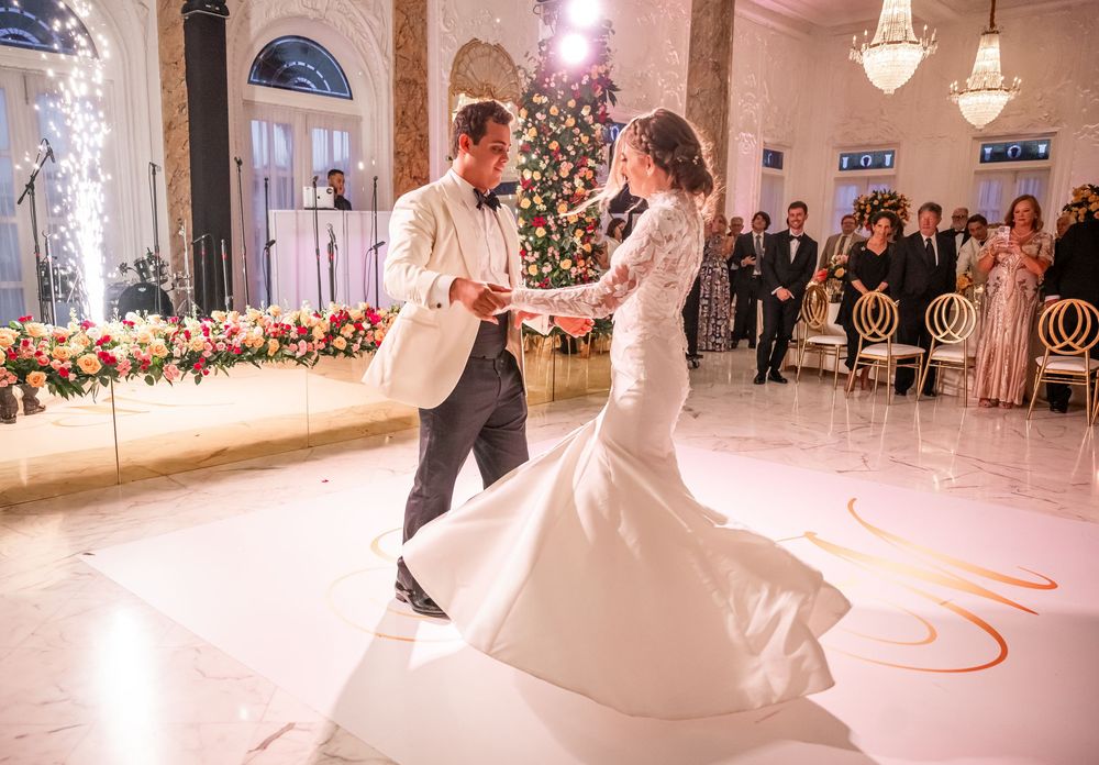 Newlywed couple shares their first dance in an elegant ballroom with crystal chandeliers and glowing lights.