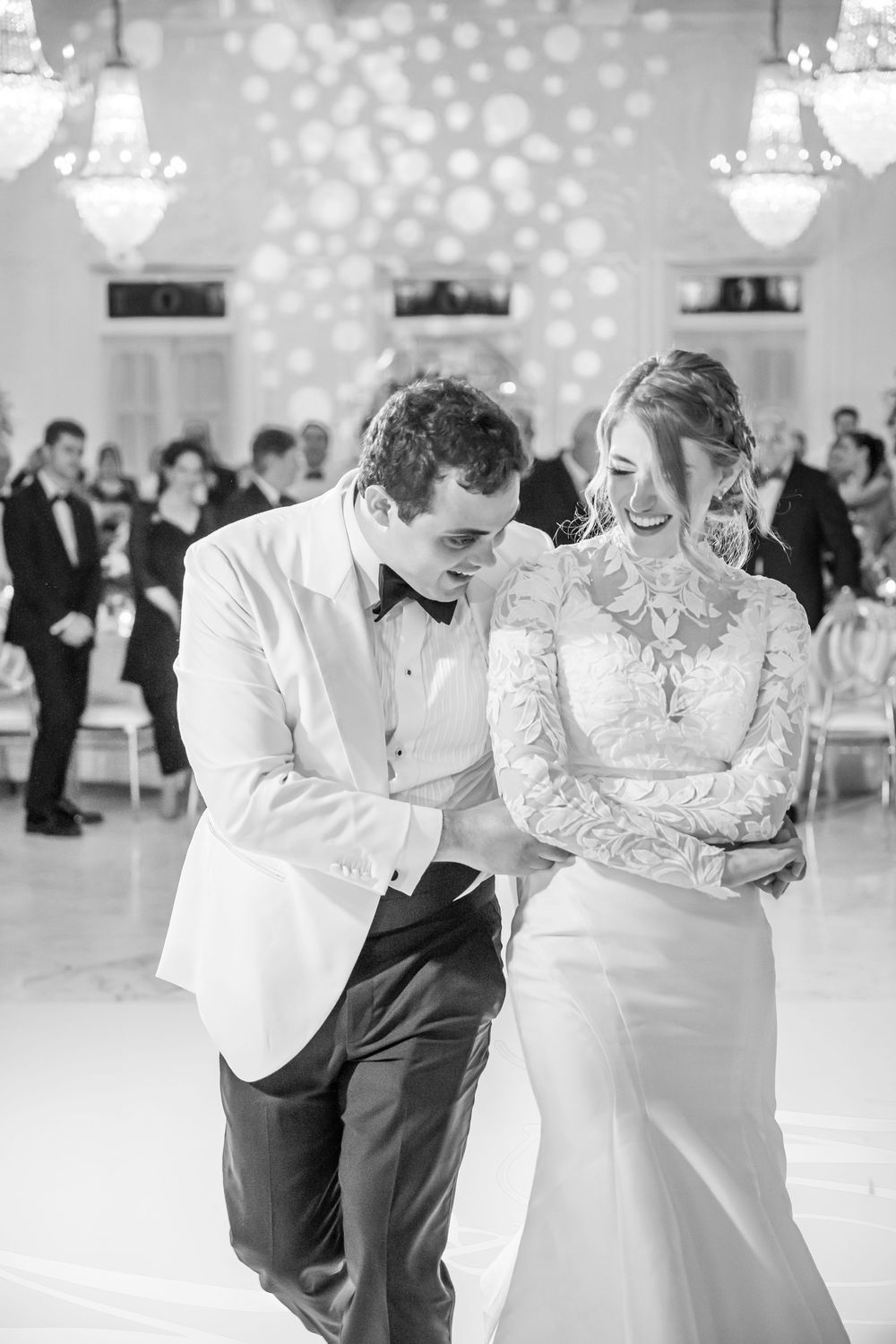 A happy couple shares a joyful moment while dancing together at their elegant wedding reception with sparkling lights.