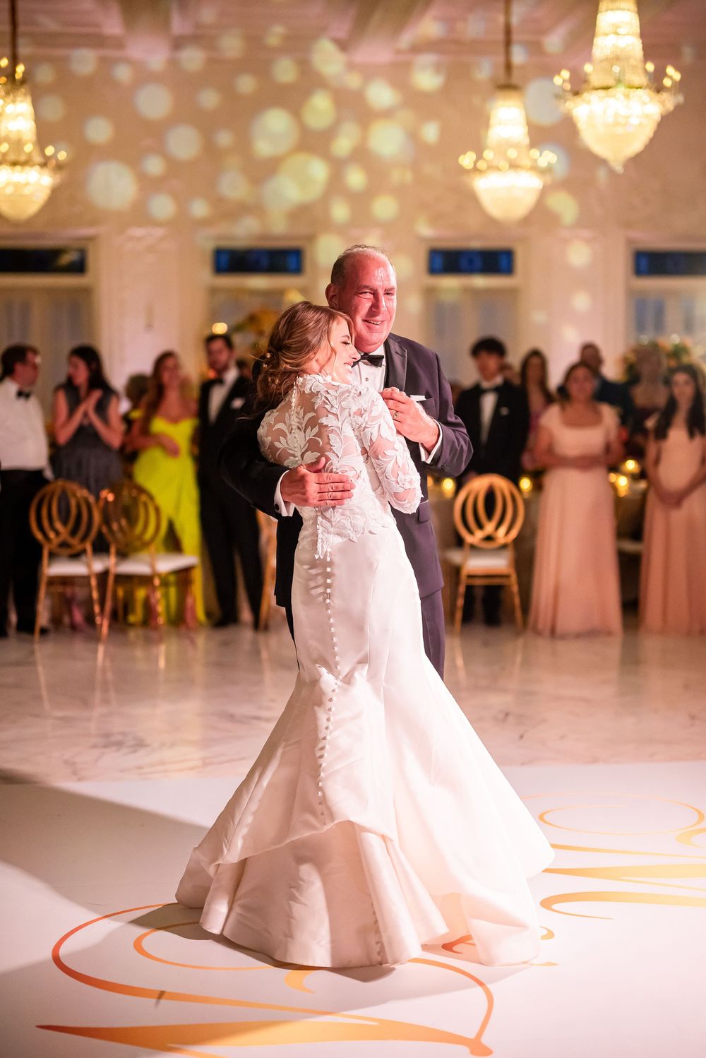 Couple sharing a romantic first dance on an elegant white dance floor with decorative orange swirls at their wedding reception.