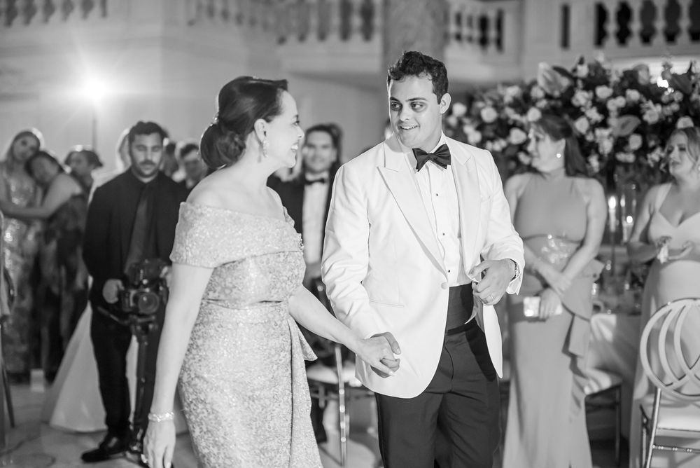 Couple in formal attire dancing at an elegant event with onlookers in the background in black and white.