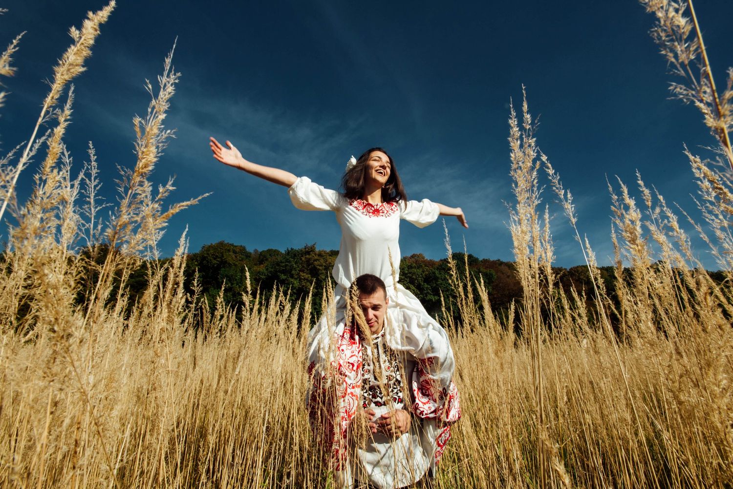 A couple in wedding attire sits together on a rustic wooden swing overlooking a scenic autumn landscape at sunset.