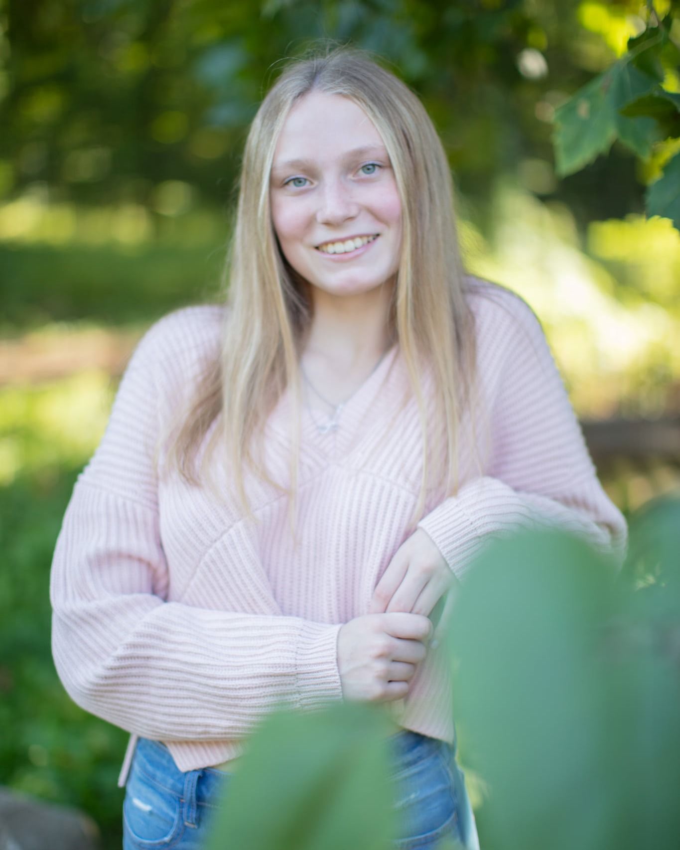 A portrait series against a green garden background shows a person smiling and posing in a cream sweater and jeans.