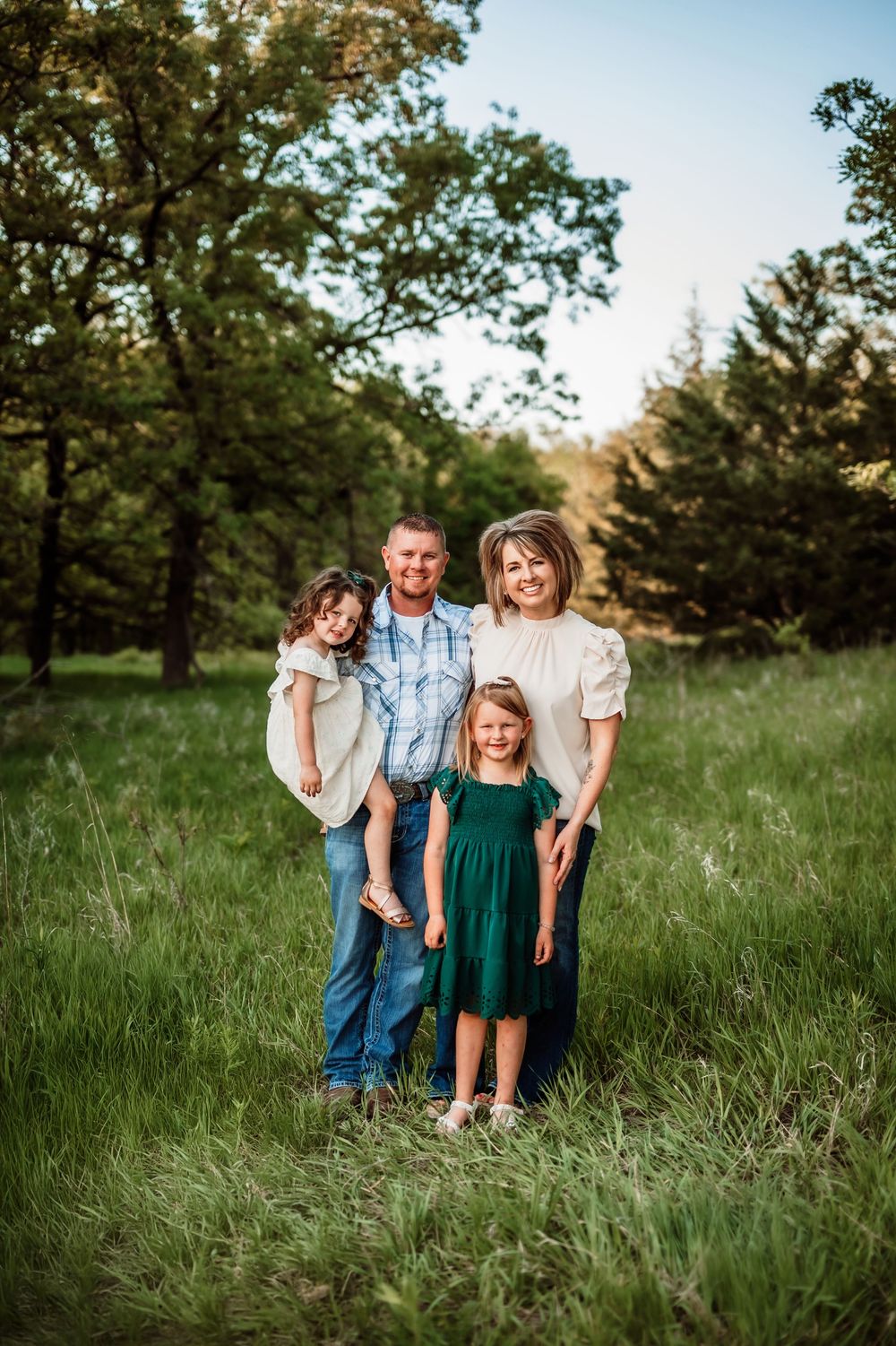 A group portrait taken outdoors in a grassy field surrounded by trees on a sunny day.