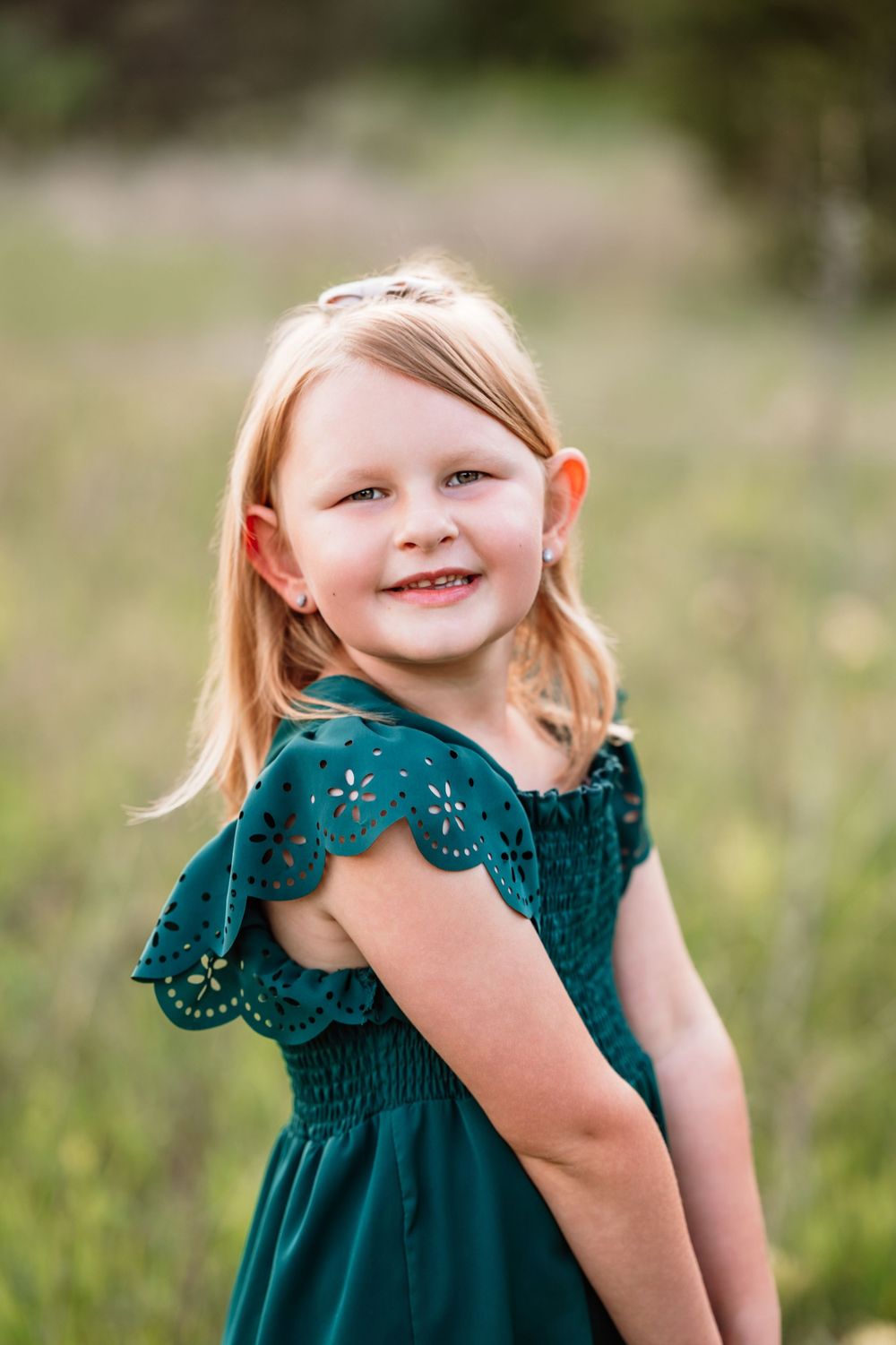 Young child wearing a dark teal dress with lace flutter sleeves poses outdoors in a natural setting.