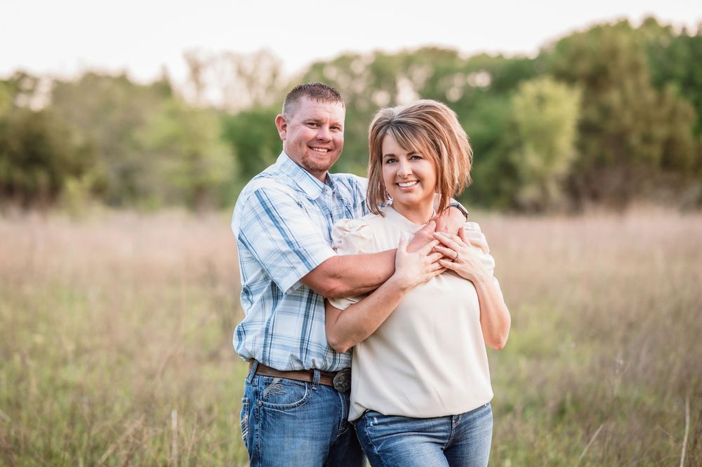 A couple smiling and embracing outdoors in a rustic field during golden hour.