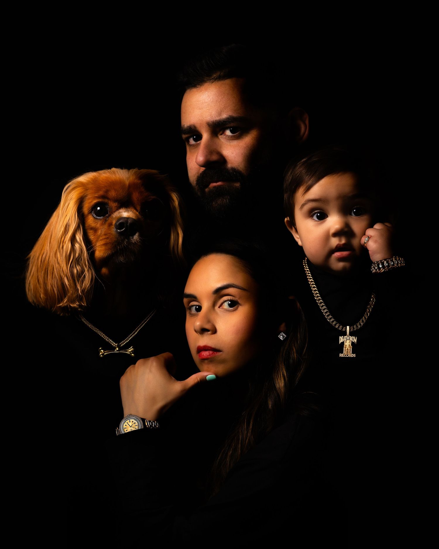 Dramatic studio portrait by Steven Marsicano with dog and family against black background posing to recreate Death Row Records photo.