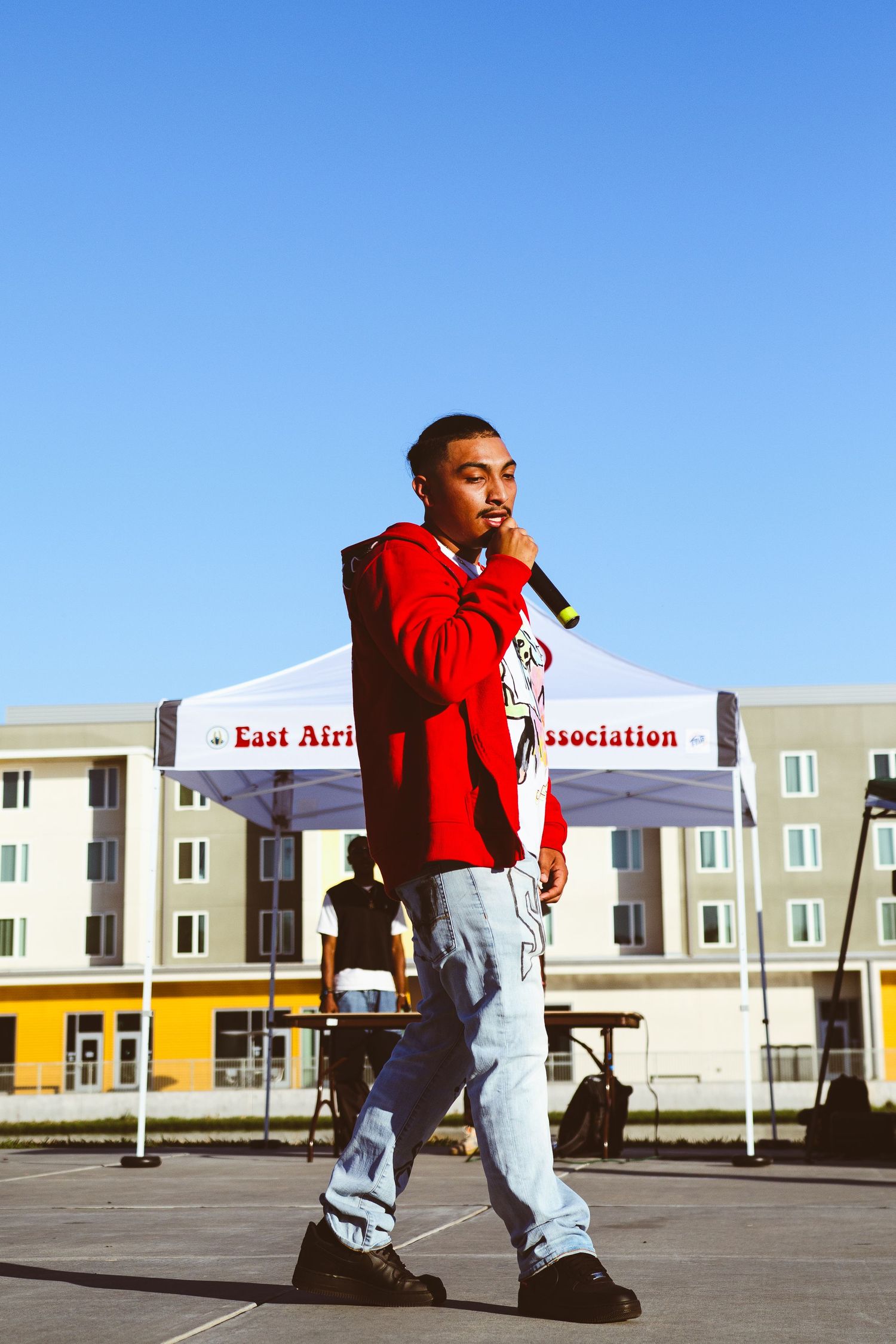 Performer in red hoodie rapping into microphone at East African Student Association outdoor event.