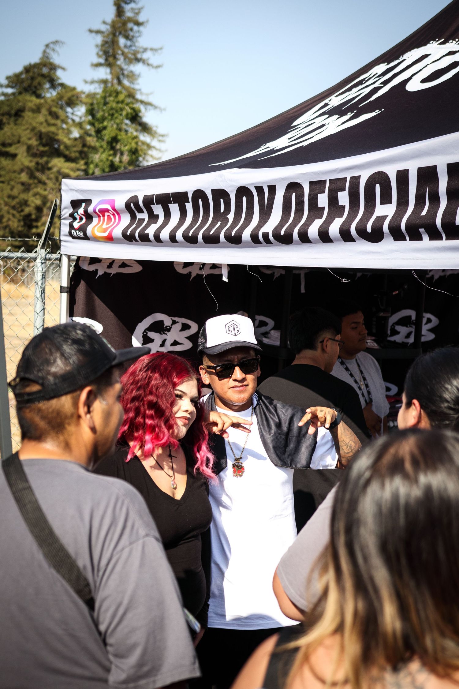 Woman with pink hair poses with a man at the Gettoboy Official vendor booth outdoors.