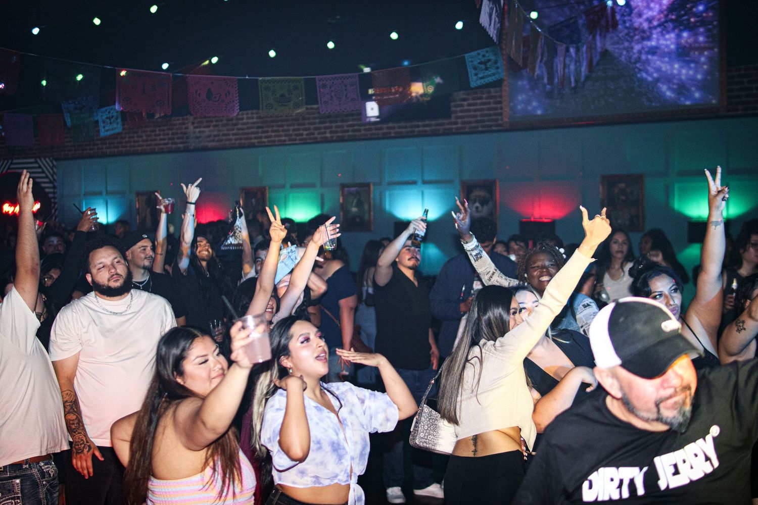 Energetic crowd dancing and raising hands at a vibrant nightclub party with colorful lights.