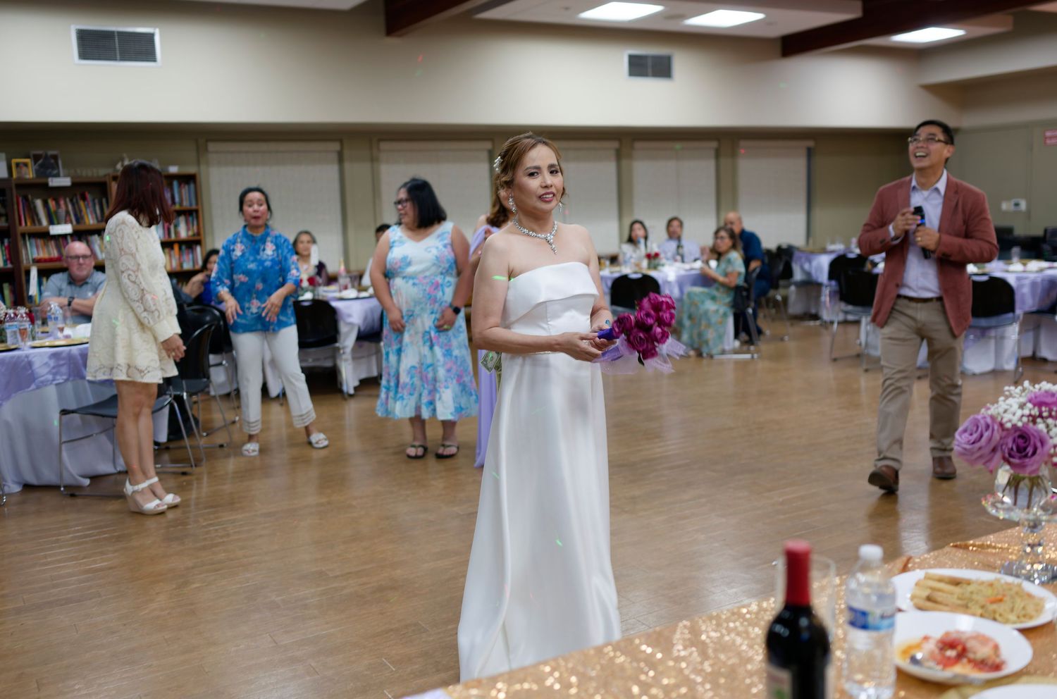 People gathered in a community center or church hall with tables and chairs set up for a social event or celebration.