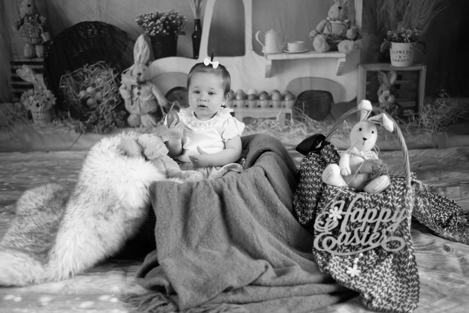 A vintage black and white photograph showing a small child with a dog and toy doll on a plush rug.