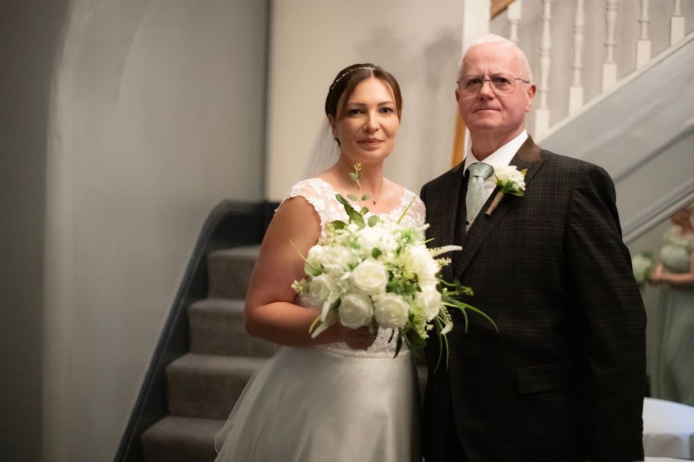 A pair at a wedding ceremony stand together on a staircase, with the bride holding a white floral bouquet.