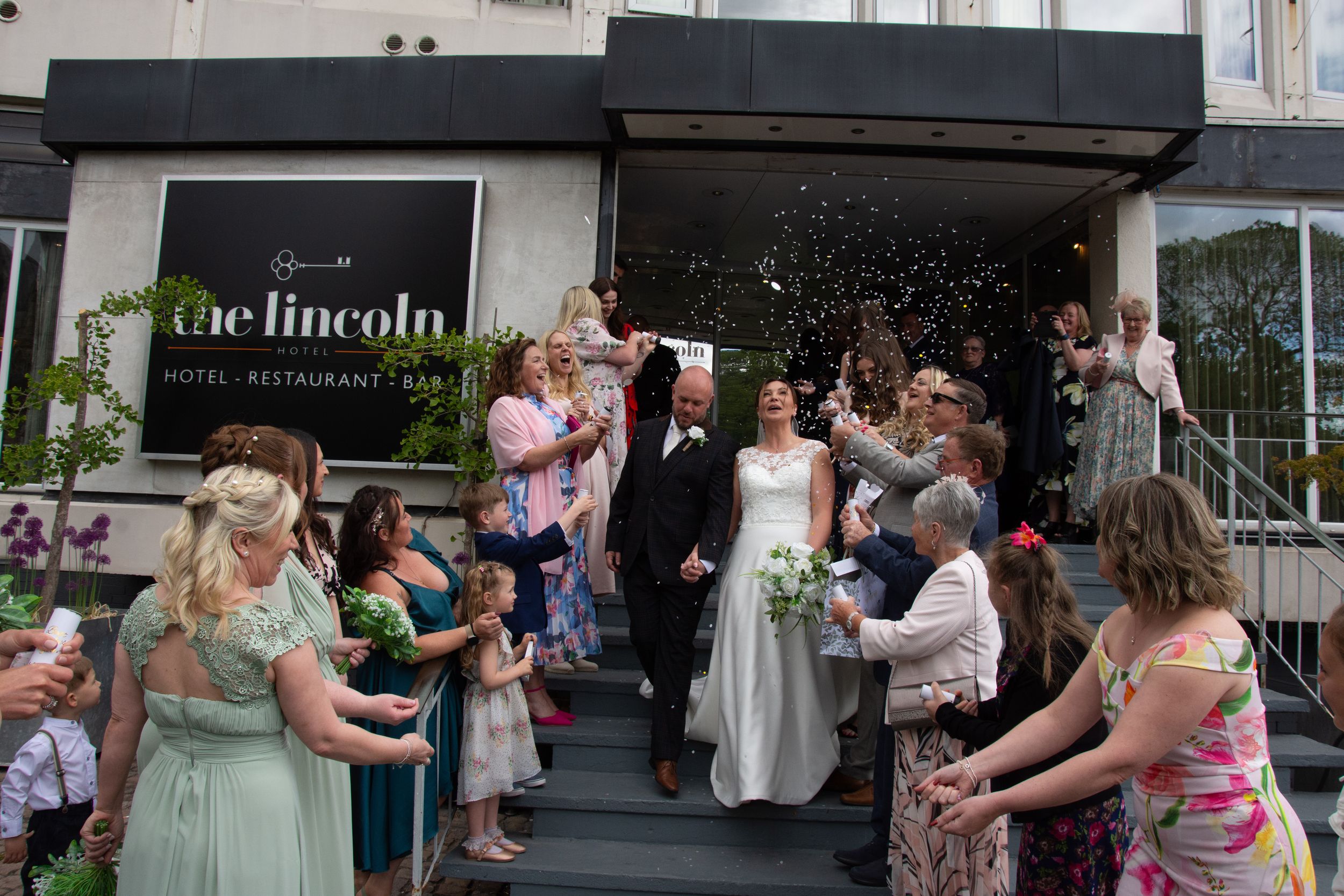 Wedding guests toss confetti at a celebratory couple exiting The Lincoln venue on their special day.