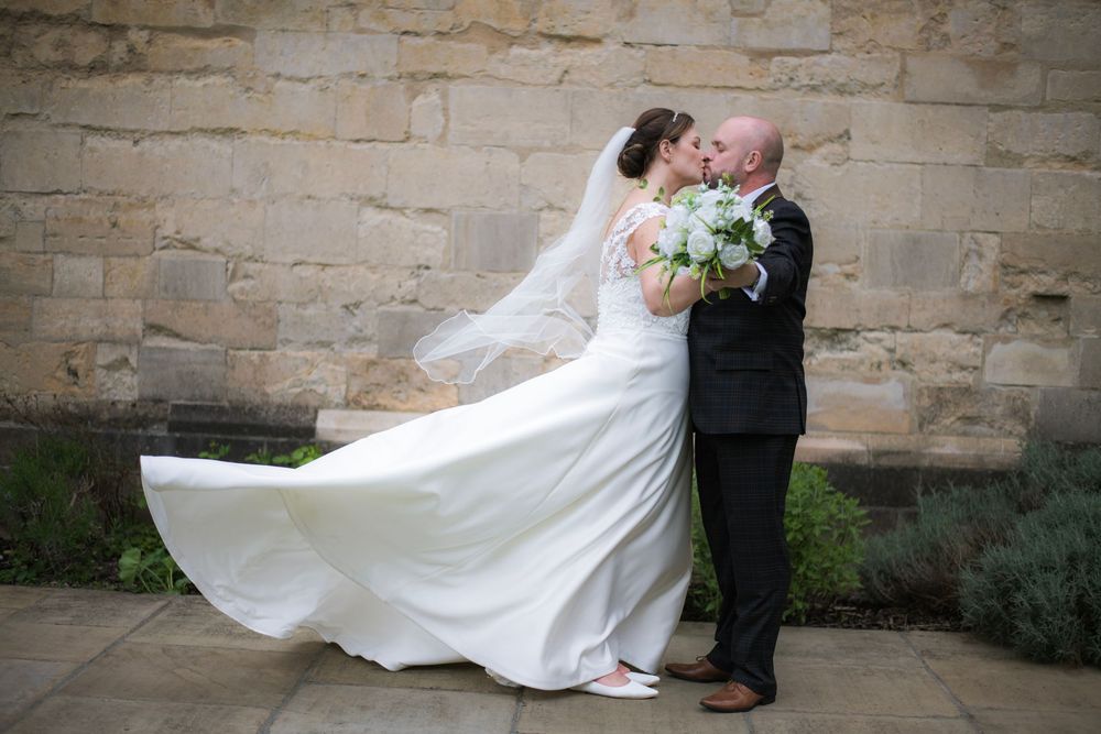 A romantic wedding portrait with flowing white dress against a stone wall backdrop during a breezy moment.