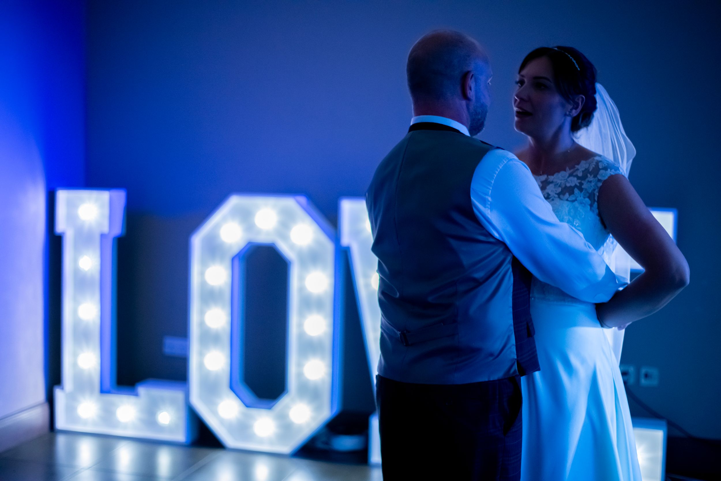 A couple shares an intimate dance moment in front of illuminated LOVE letters at their wedding reception.