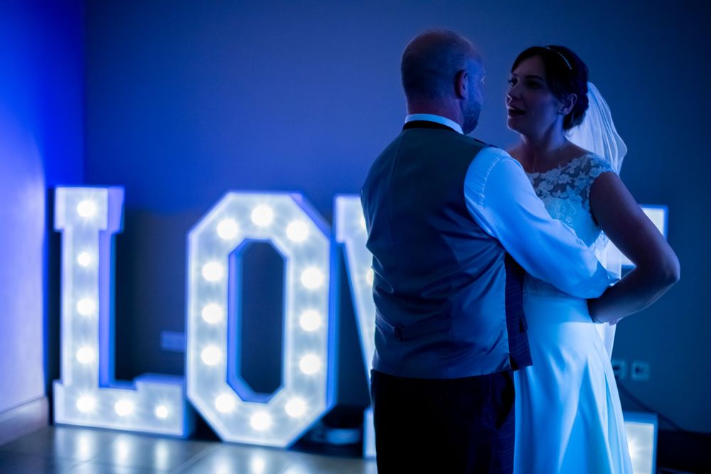 A couple shares an intimate dance moment in front of illuminated LOVE letters at their wedding reception.