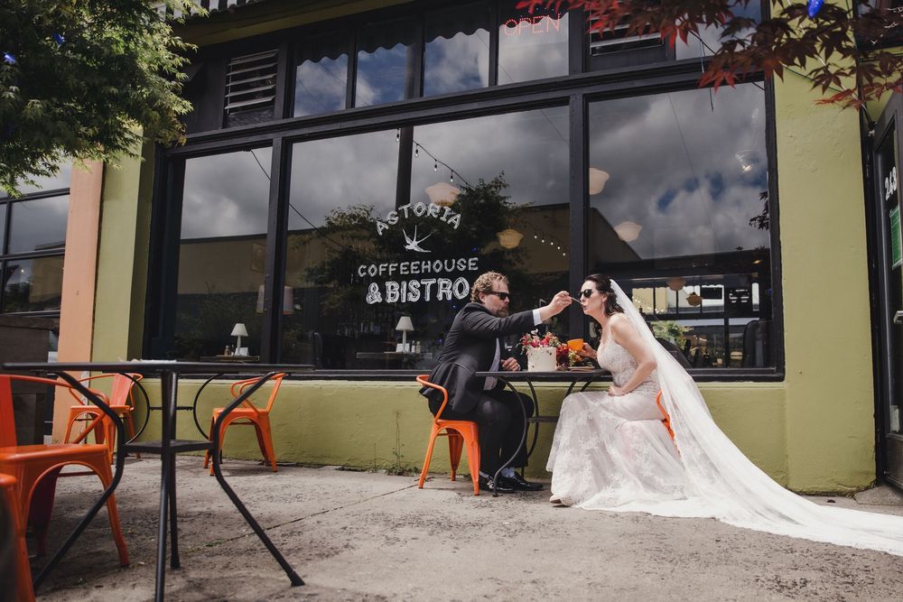 Bride and groom toasting at outdoor cafe table in front of Victoria Coffeehouse and Bistro on their wedding day.