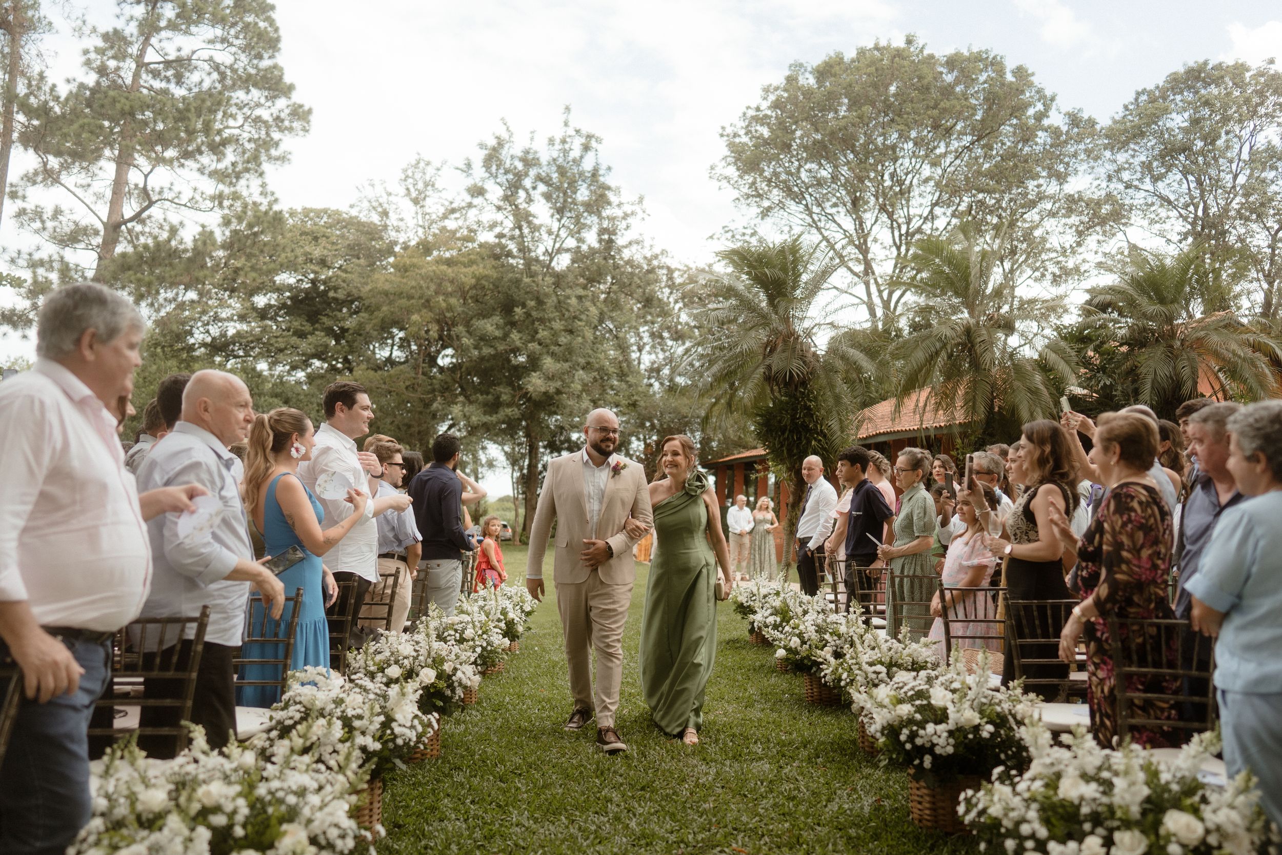 Wedding ceremony aisle decorated with white flowers as guests stand on both sides.