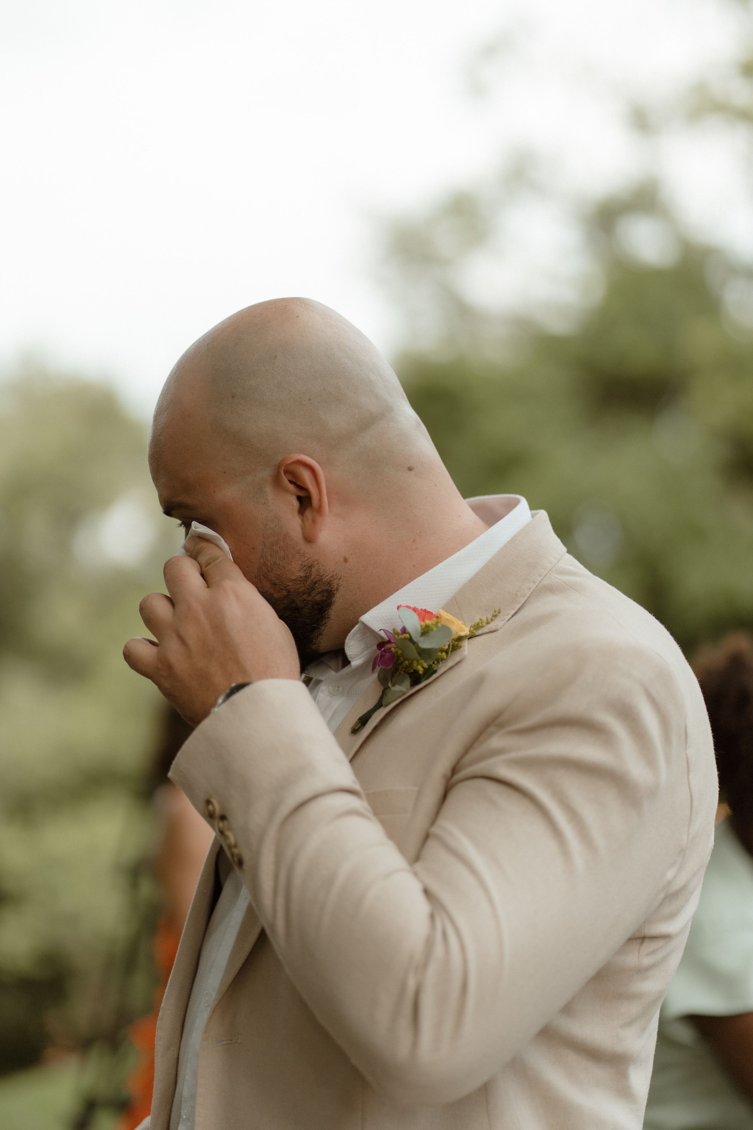 Touching candid moment during outdoor wedding ceremony with floral boutonniere.