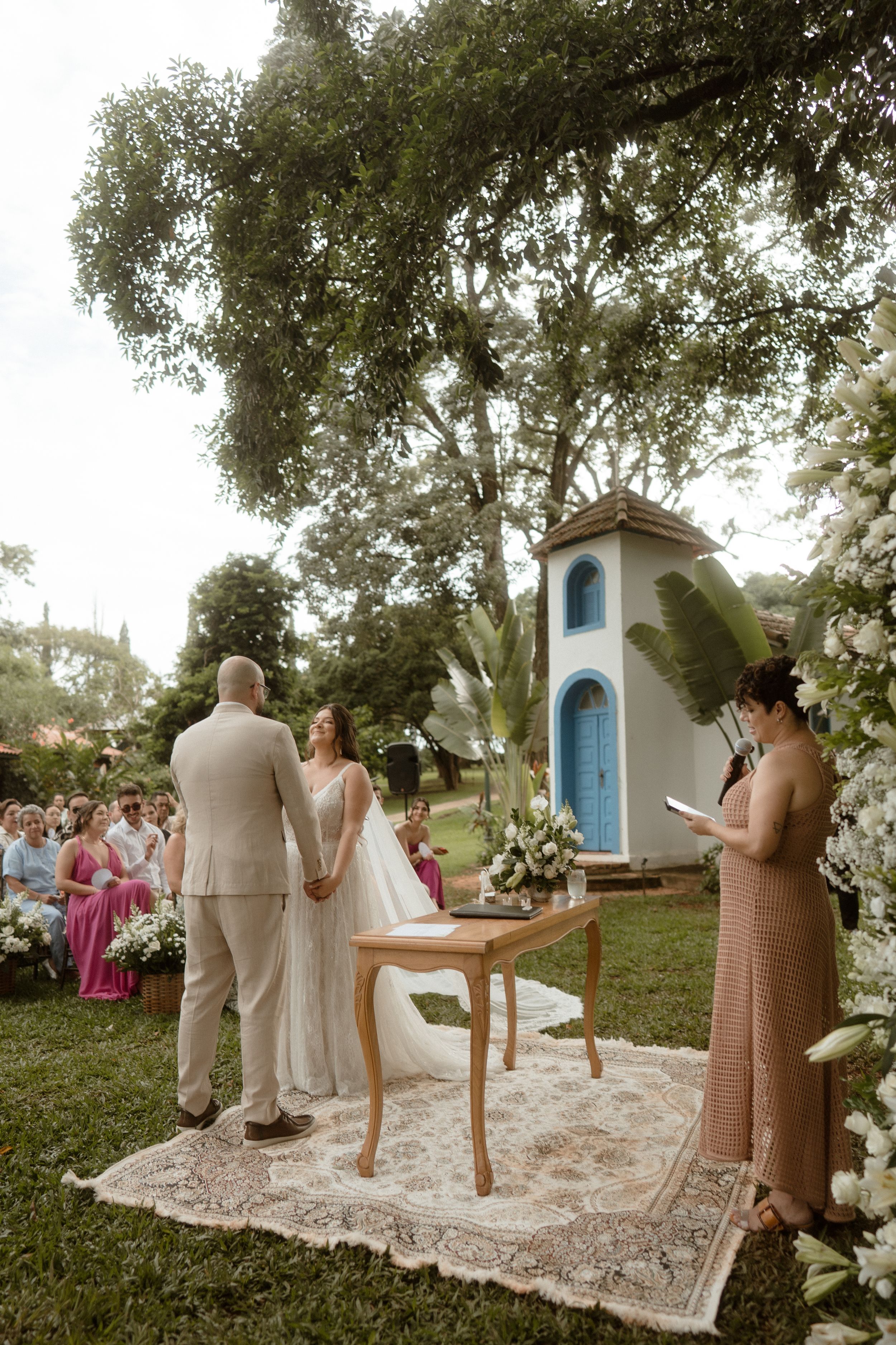 A rustic outdoor wedding ceremony setup with a small blue chapel structure and floral decorations.