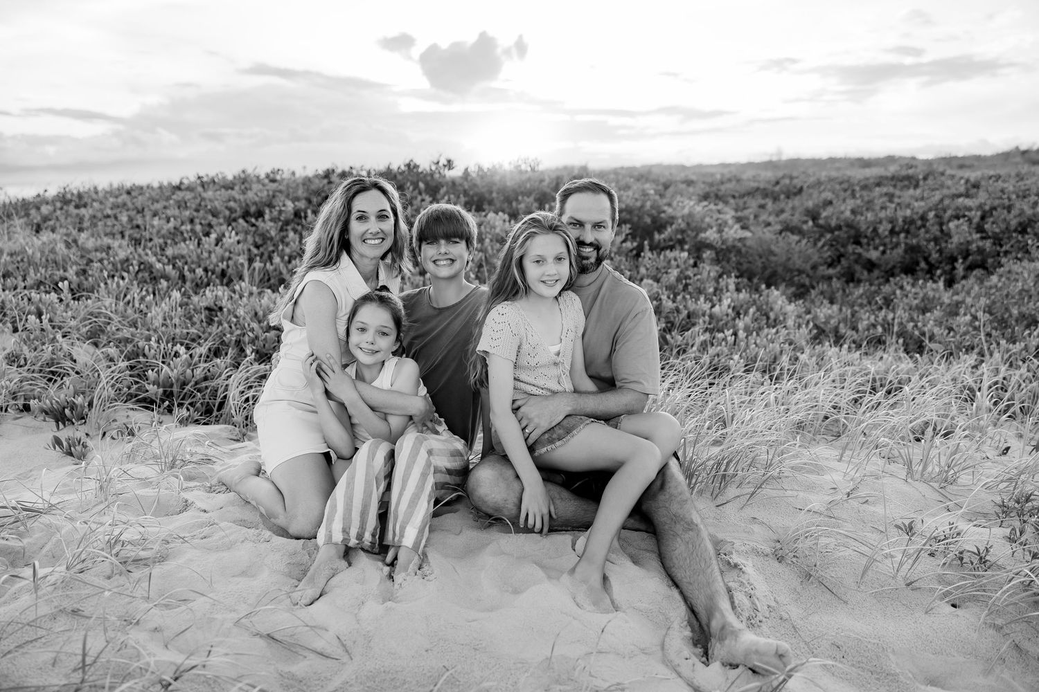 A joyful family moment captured in black and white as they sit together in a sunlit field.