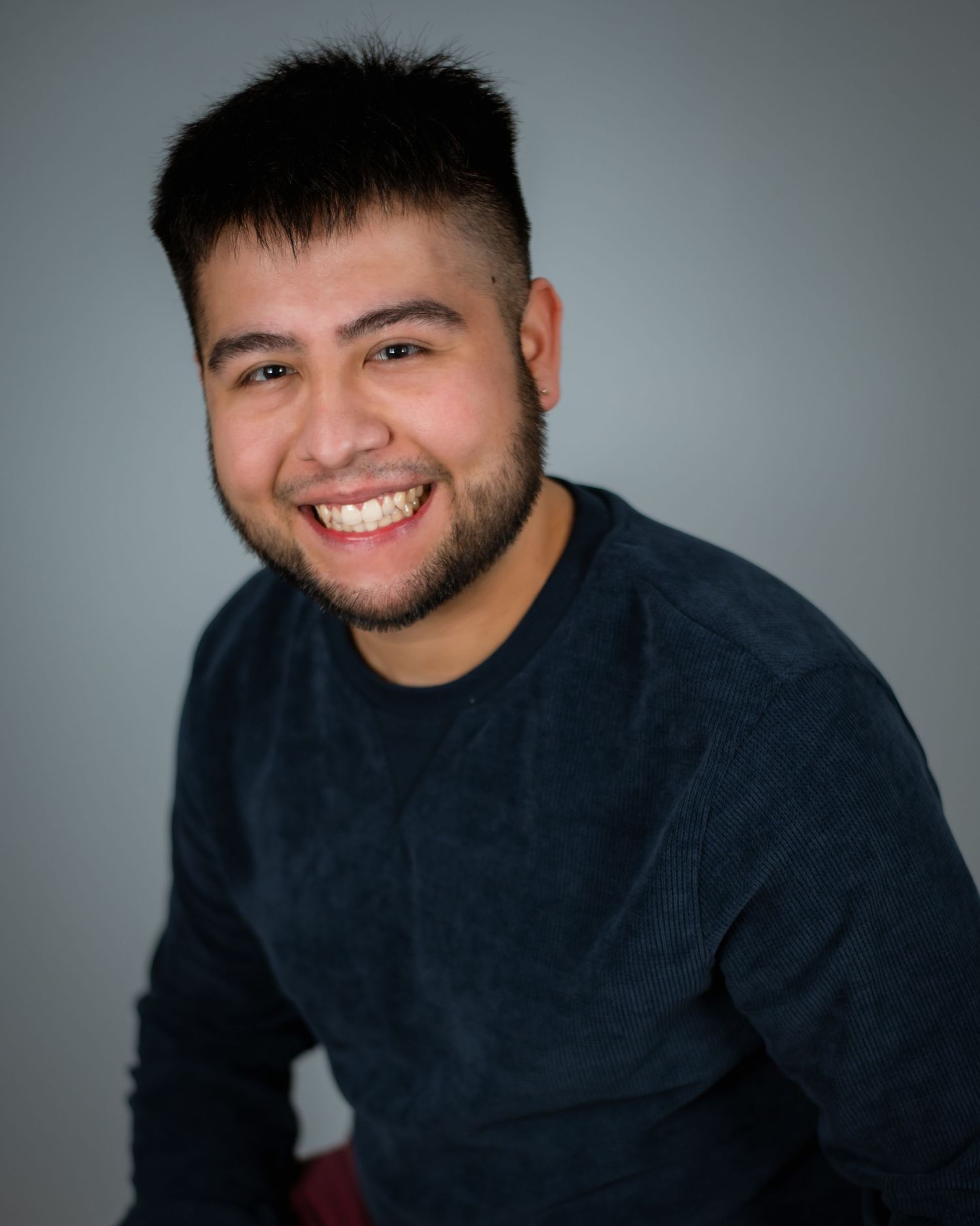 Professional headshot of someone in a dark blue sweater smiling warmly against a gray background.