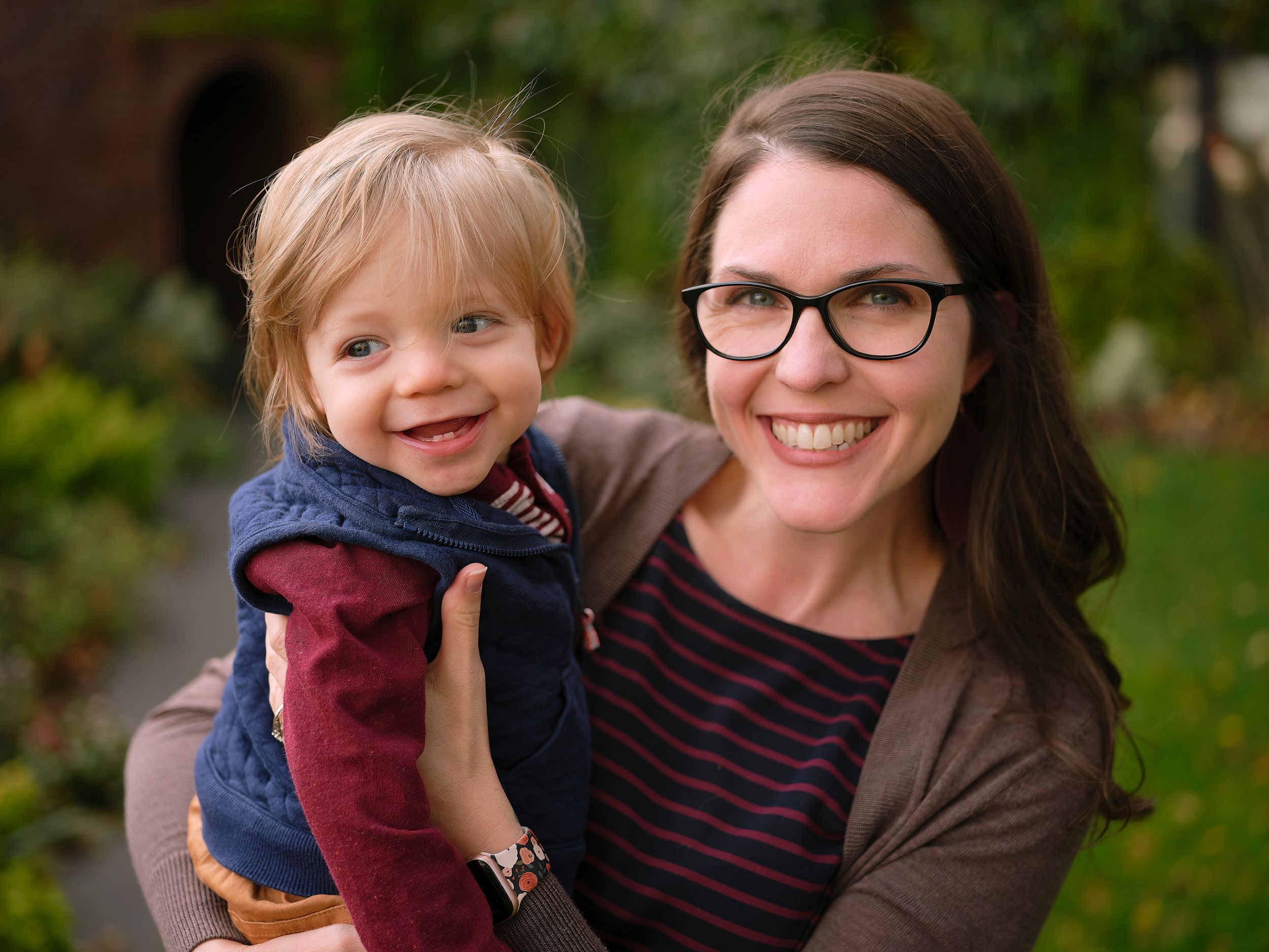 A happy portrait of parent and young child outdoors with natural greenery in the background.