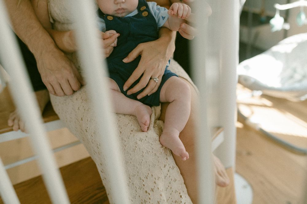 Small hands rest gently on a soft cotton blanket in warm sunlight streaming through white railings.