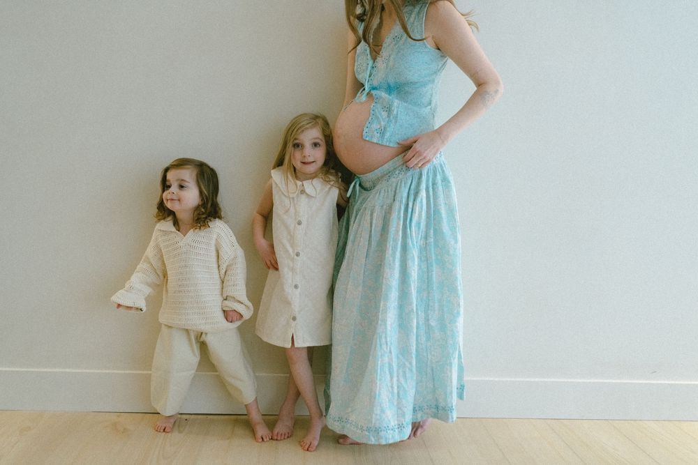 Three people in coordinating neutral and light blue outfits stand together against a white wall indoors.