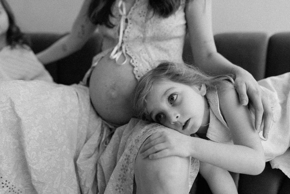 A child rests their head on a person's lap in an intimate black and white portrait.