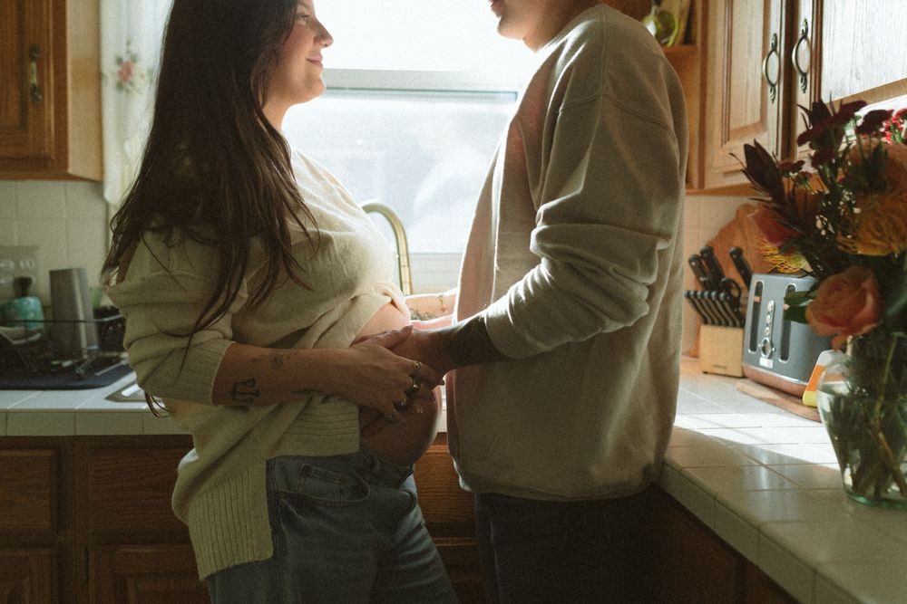 A couple shares an intimate moment together in a sunlit kitchen by the window.
