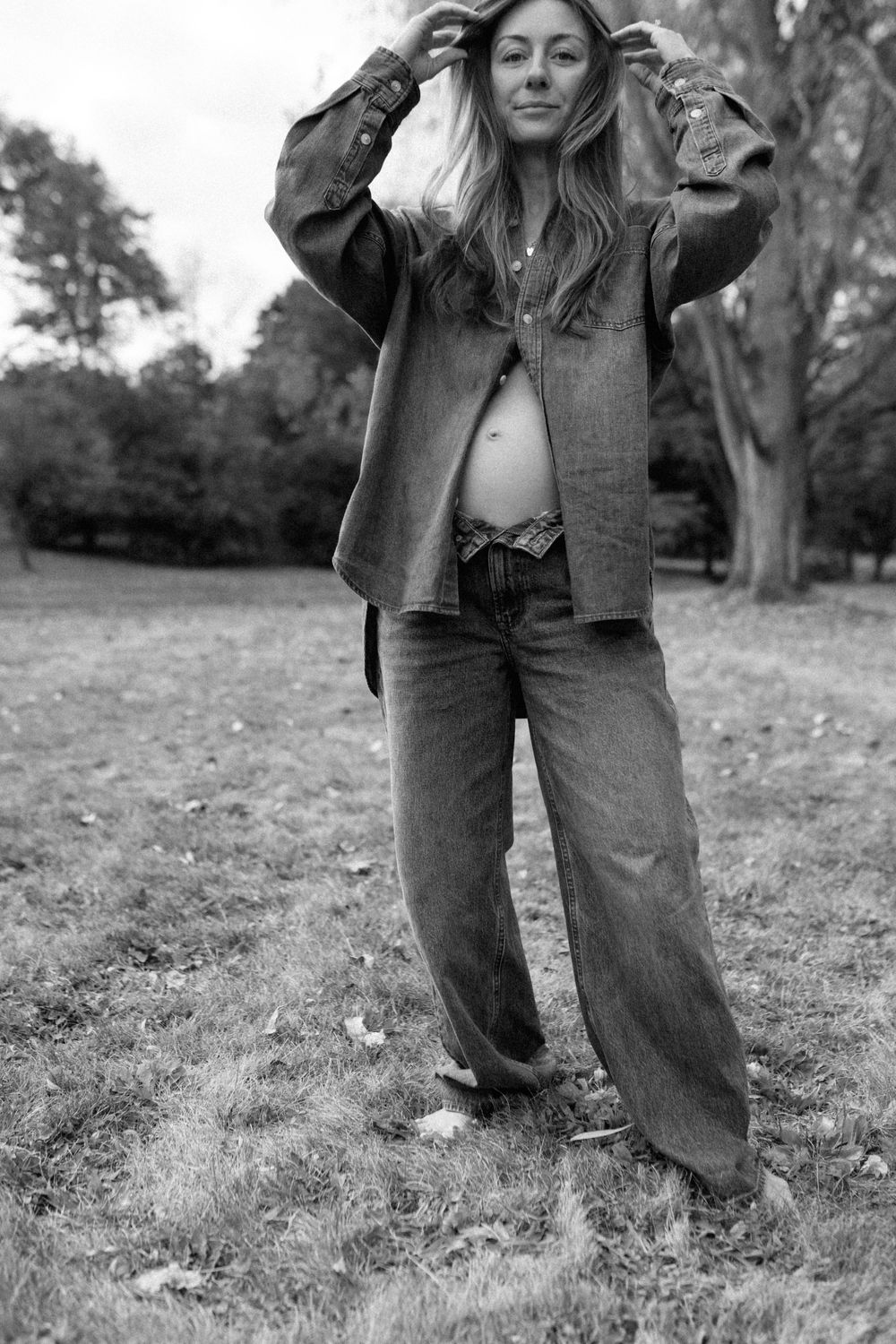 Black and white photograph showing legs wearing baggy denim jeans and boots standing in a grassy field.
