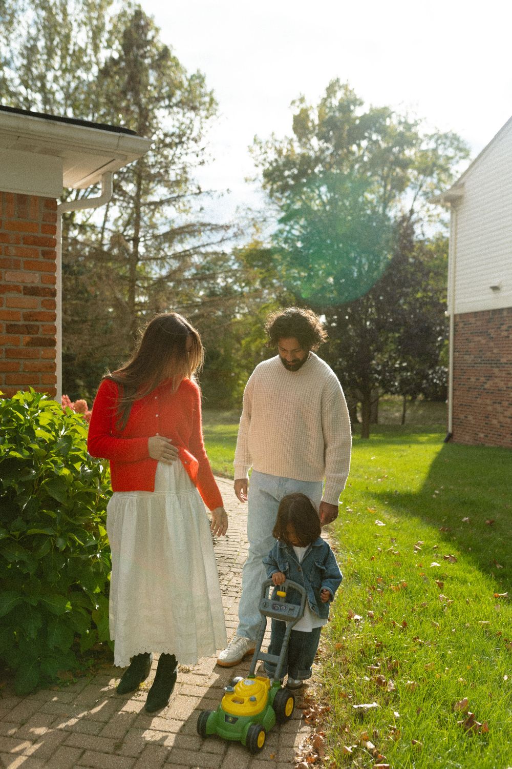 Family playing together with a toy lawn mower in a backyard garden during golden hour sunlight.