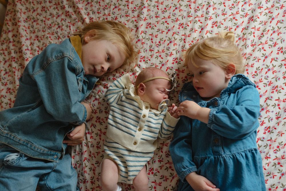 Two small children in denim and stripes share sweet moments together against a floral wallpaper background.
