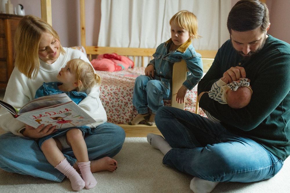 Family members sit together on floor sharing tender moments while reading and bonding at home.
