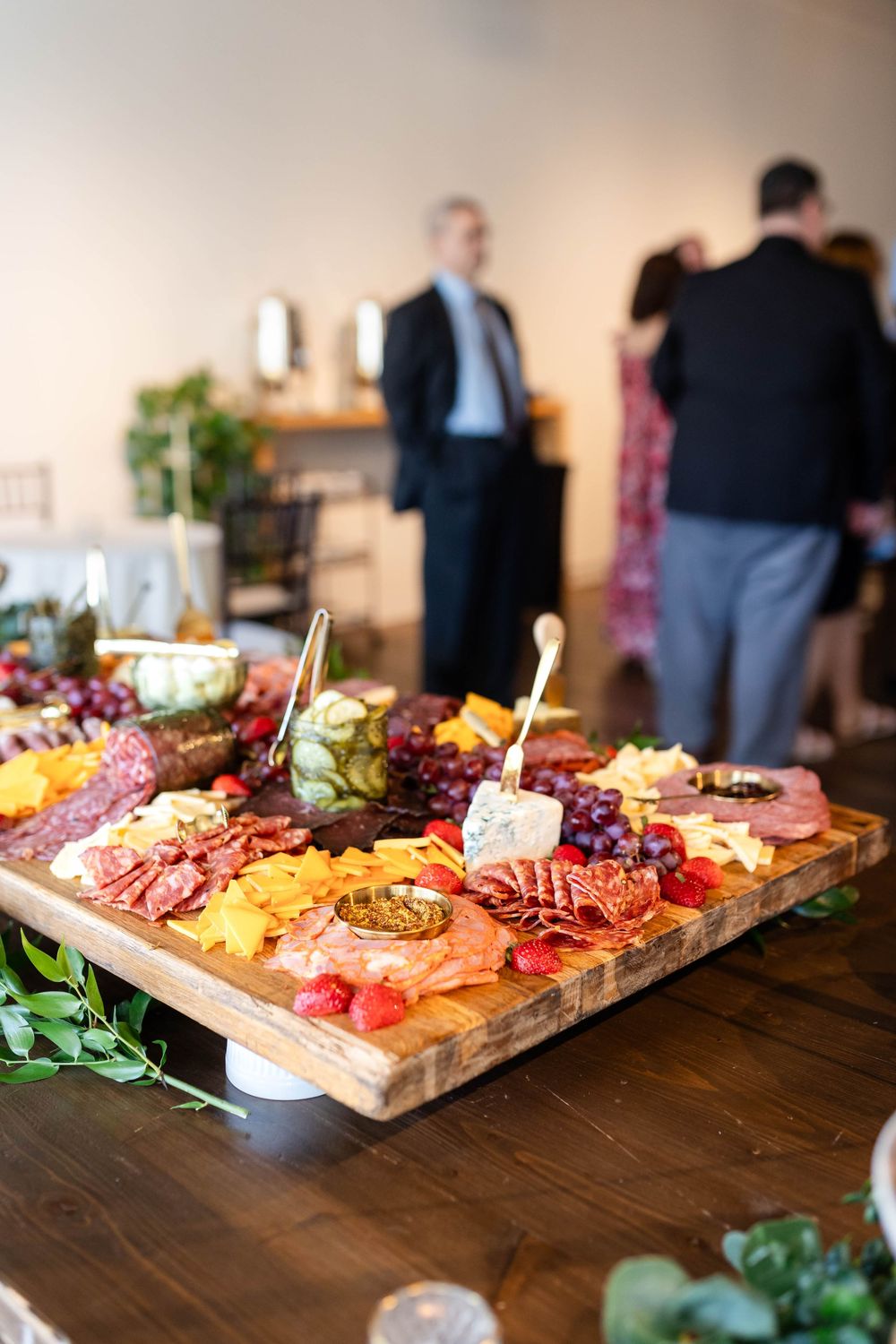 A lavish charcuterie board filled with meats, cheeses, fruits and nuts displayed on a wooden surface at an event.