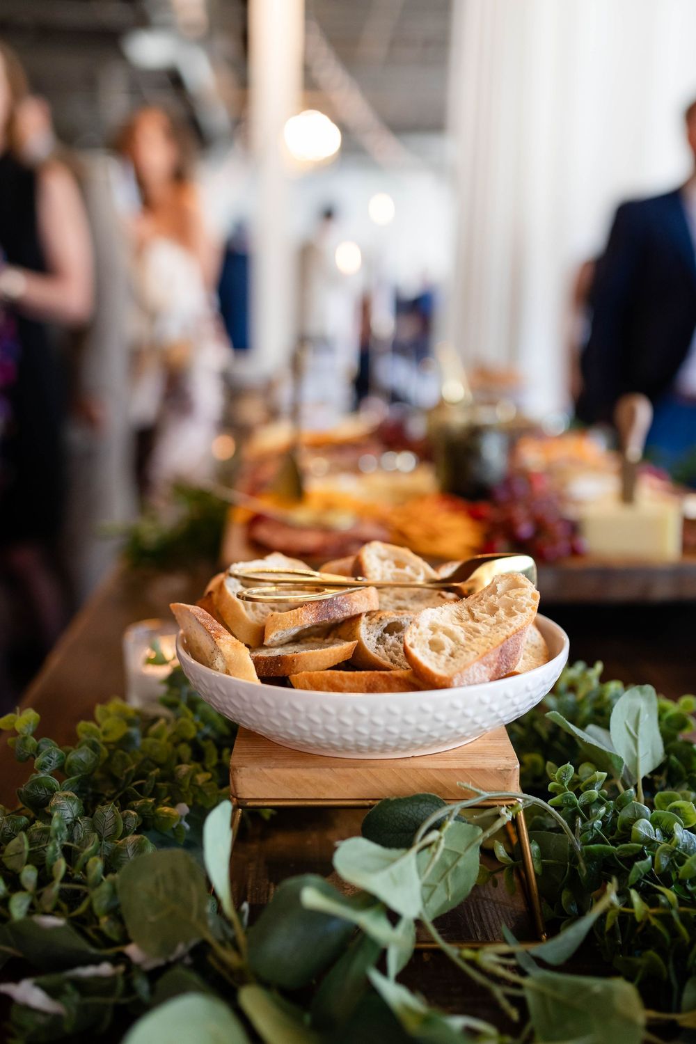 Artfully plated appetizers on a white textured dish surrounded by fresh green garnishes and herbs.