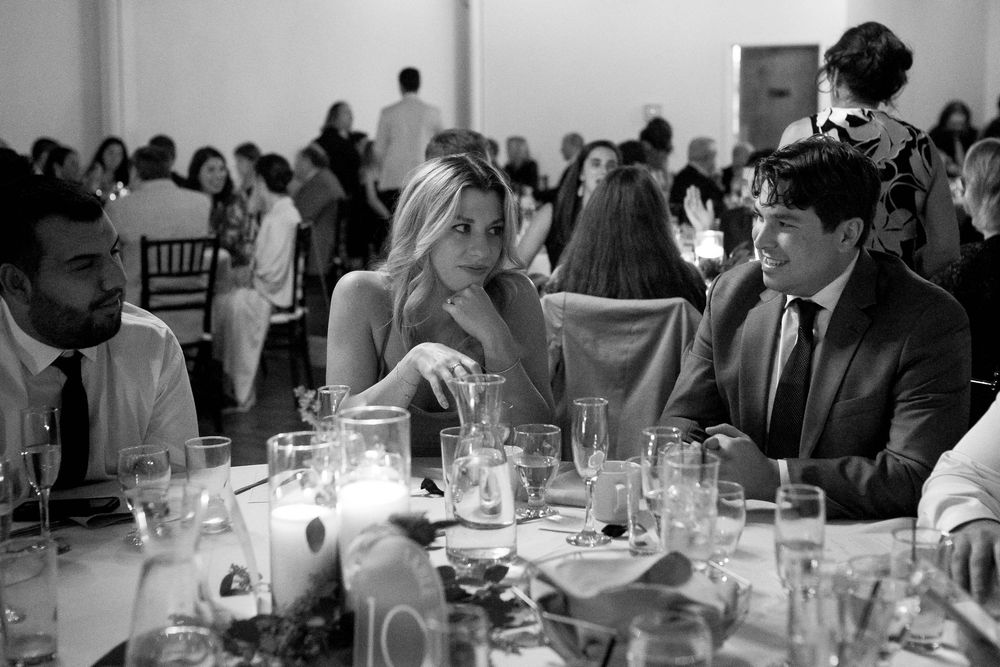 Black and white photo of people seated at an elegant dinner reception with glassware and candles on the tables.