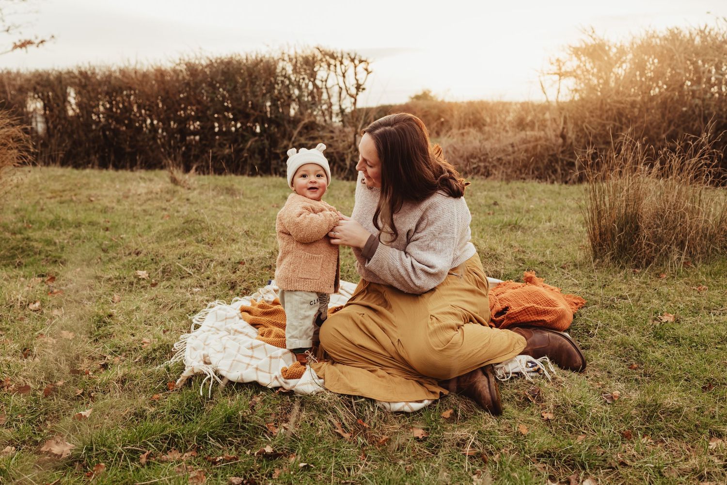 Two people share a tender moment while sitting on a blanket in a golden autumn meadow at sunset.