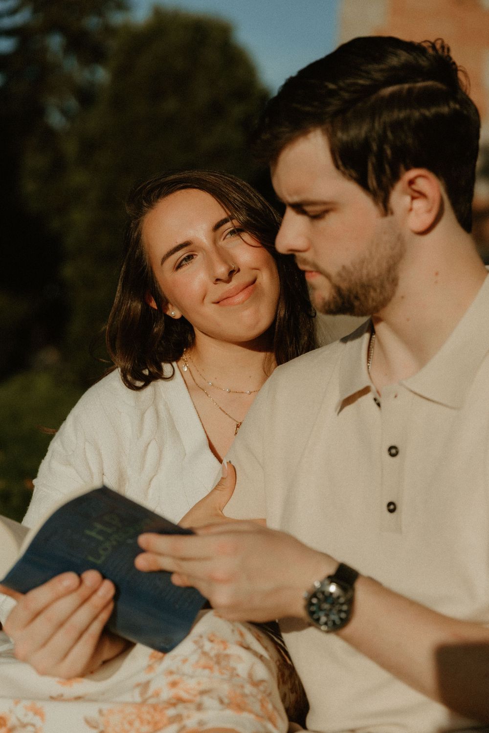 A couple in white outfits sharing an intimate moment while reading together outdoors.