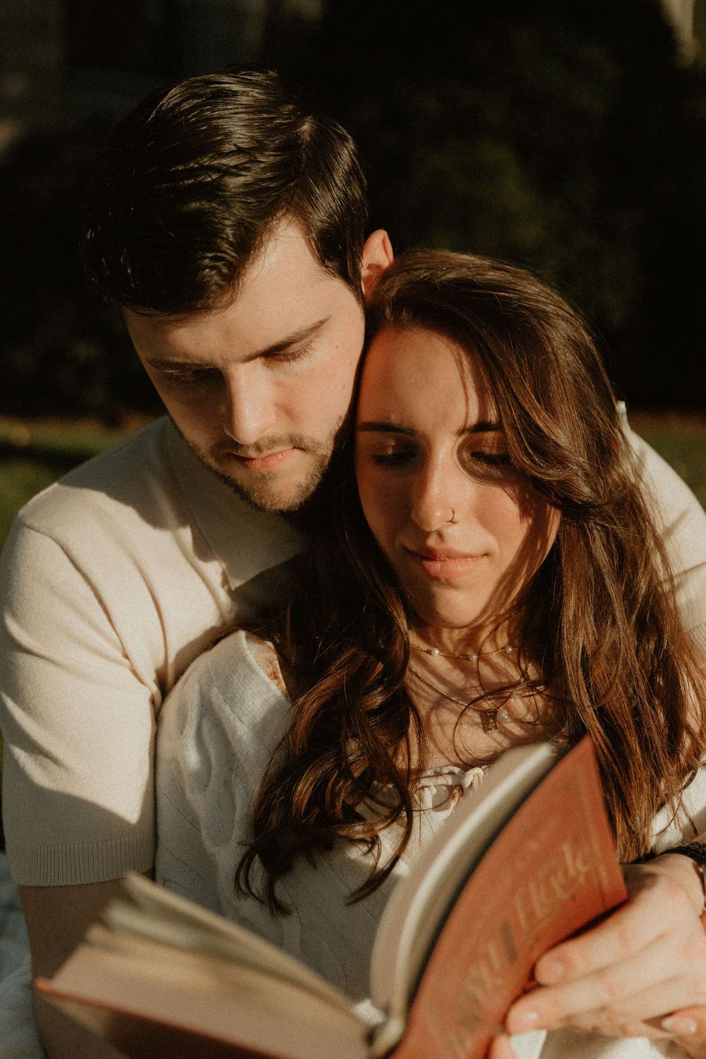 A romantic couple embraces while reading a book together in warm evening light.