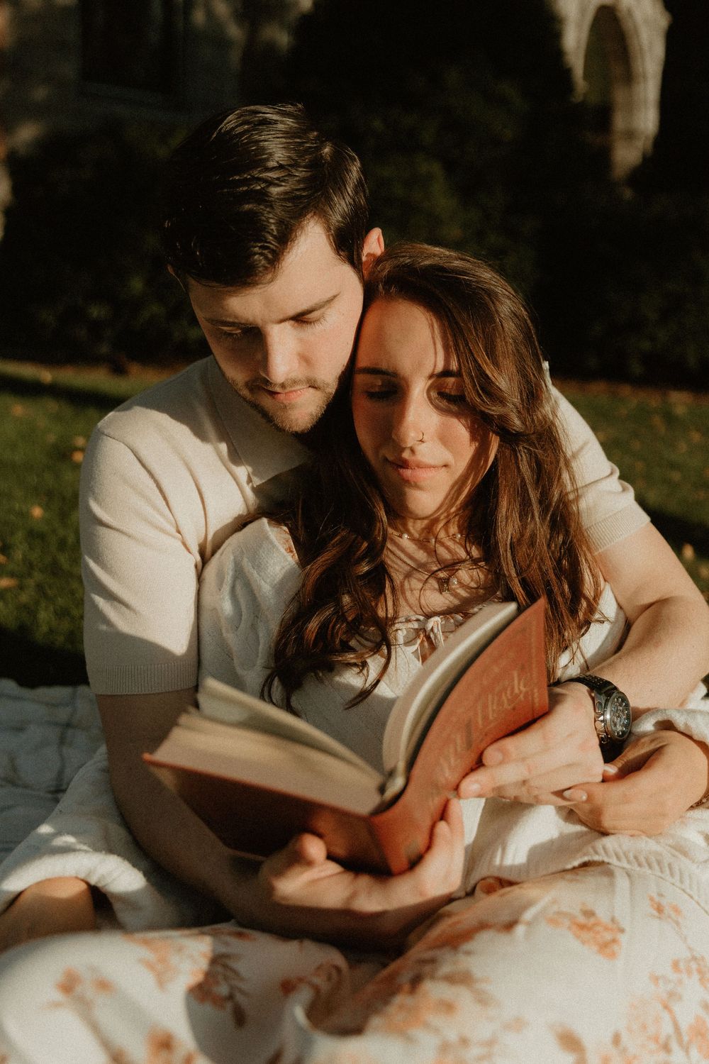 Two people share a quiet moment reading together on a blanket in golden sunlight.