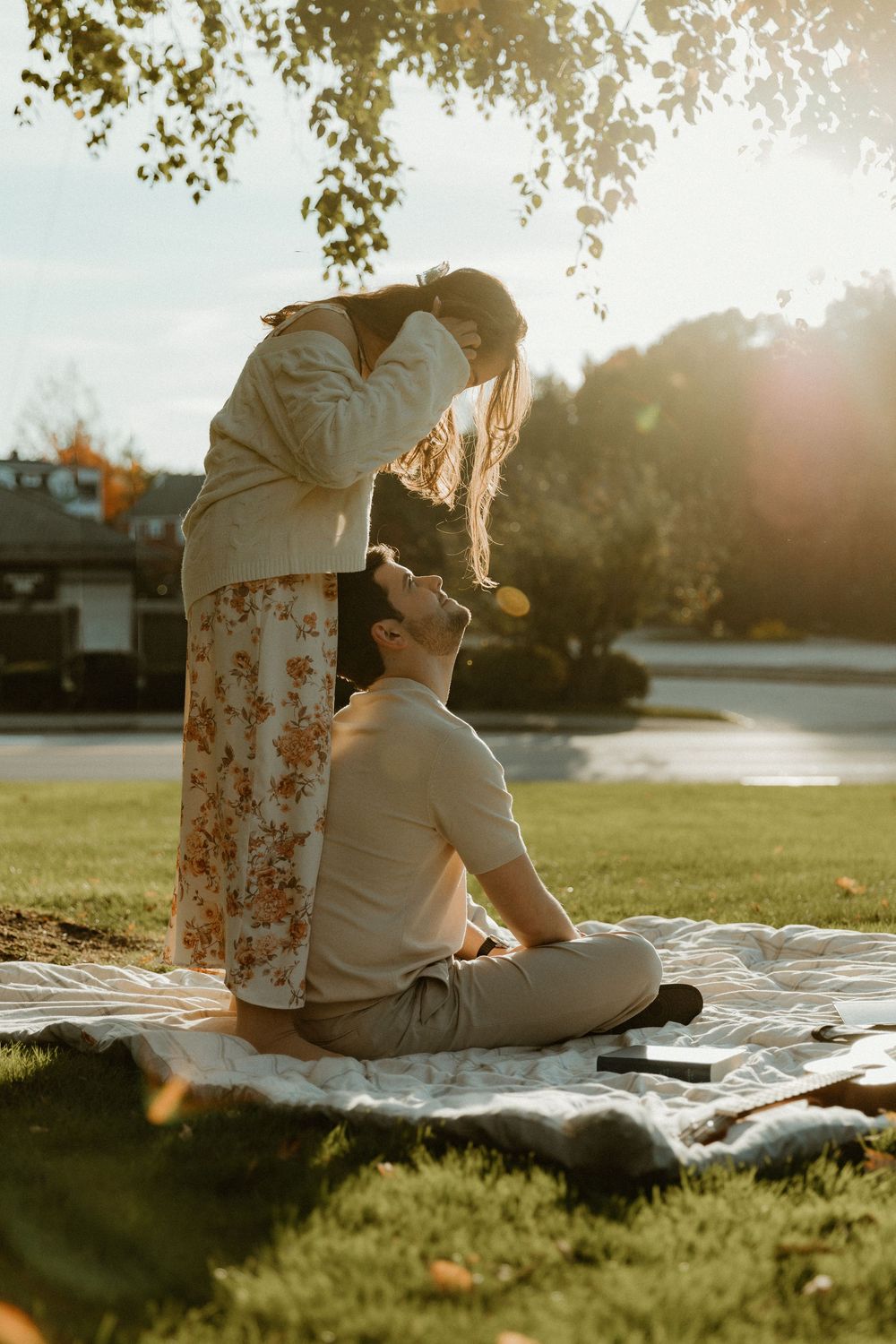 A couple sits on a blanket during sunset in a grassy park setting.