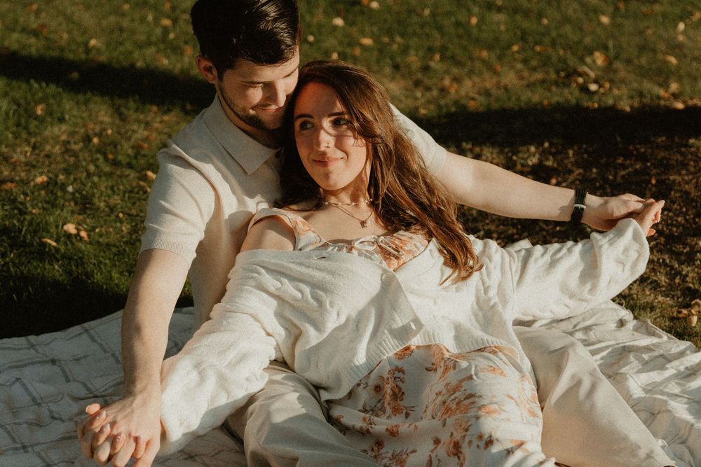 A couple shares a tender embrace while sitting on a blanket during golden hour.