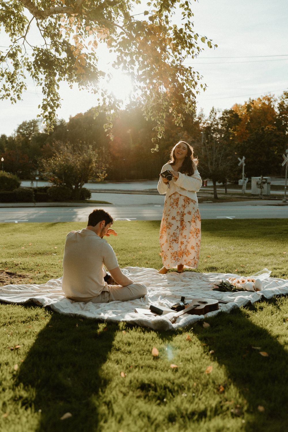 A couple enjoys a romantic sunset picnic on a blanket spread out on a grassy lawn.
