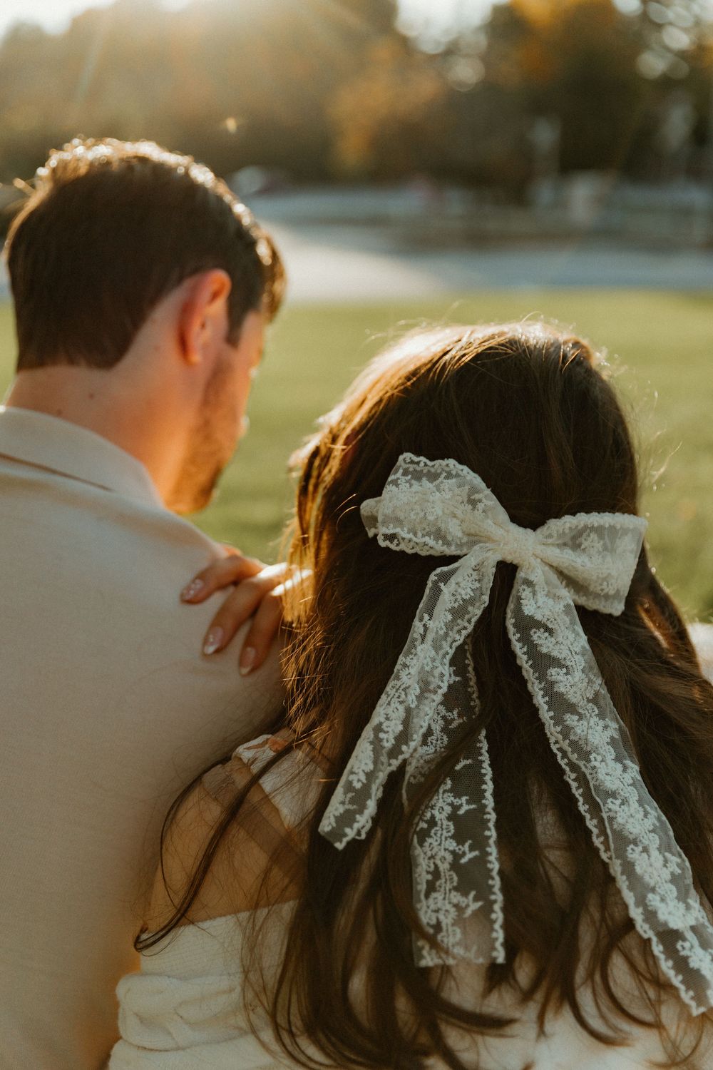 A close-up detail shot of a delicate white lace bow in long dark hair during a sunset photoshoot.