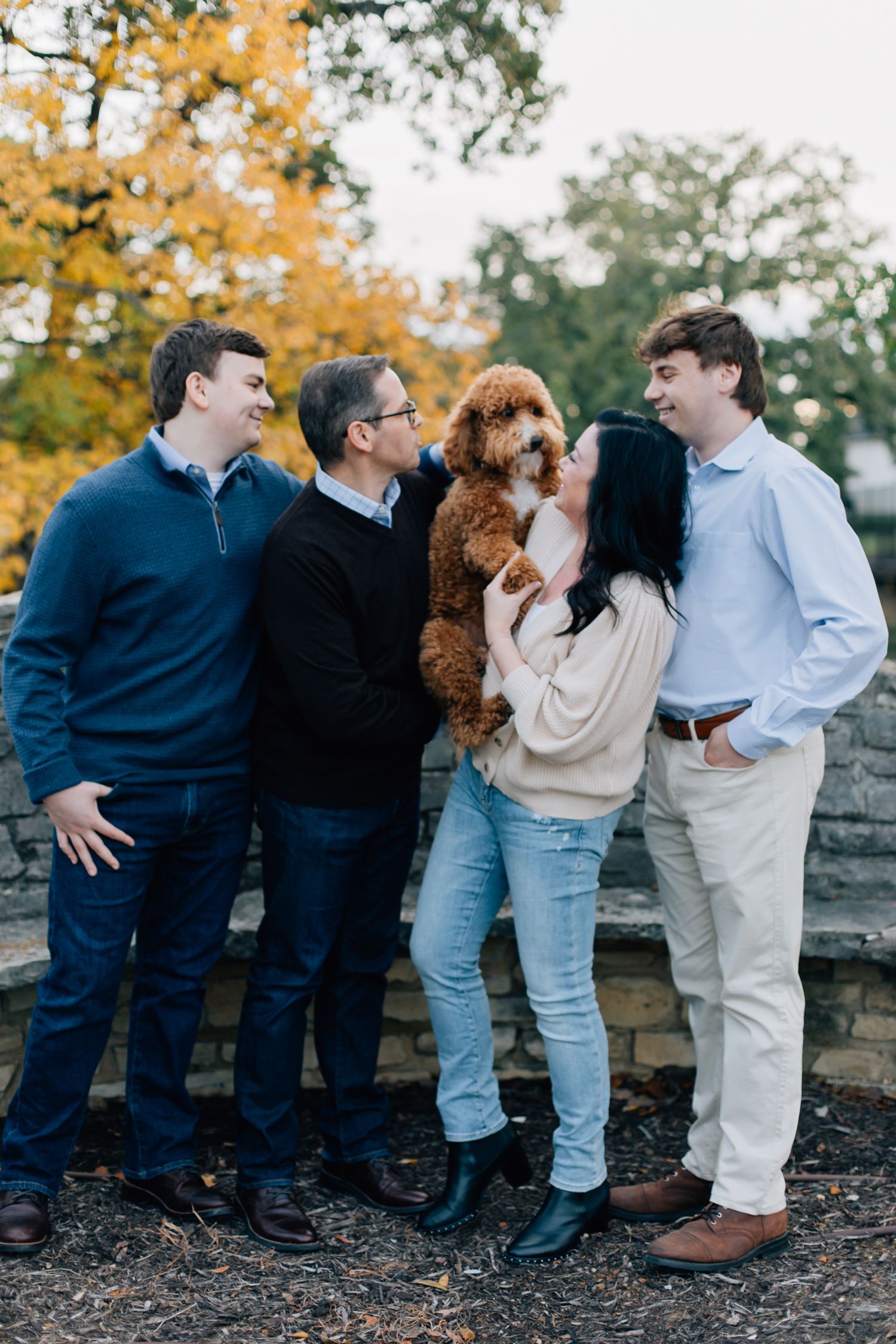 Group standing outdoors in fall with a fluffy brown goldendoodle dog being held in the middle.