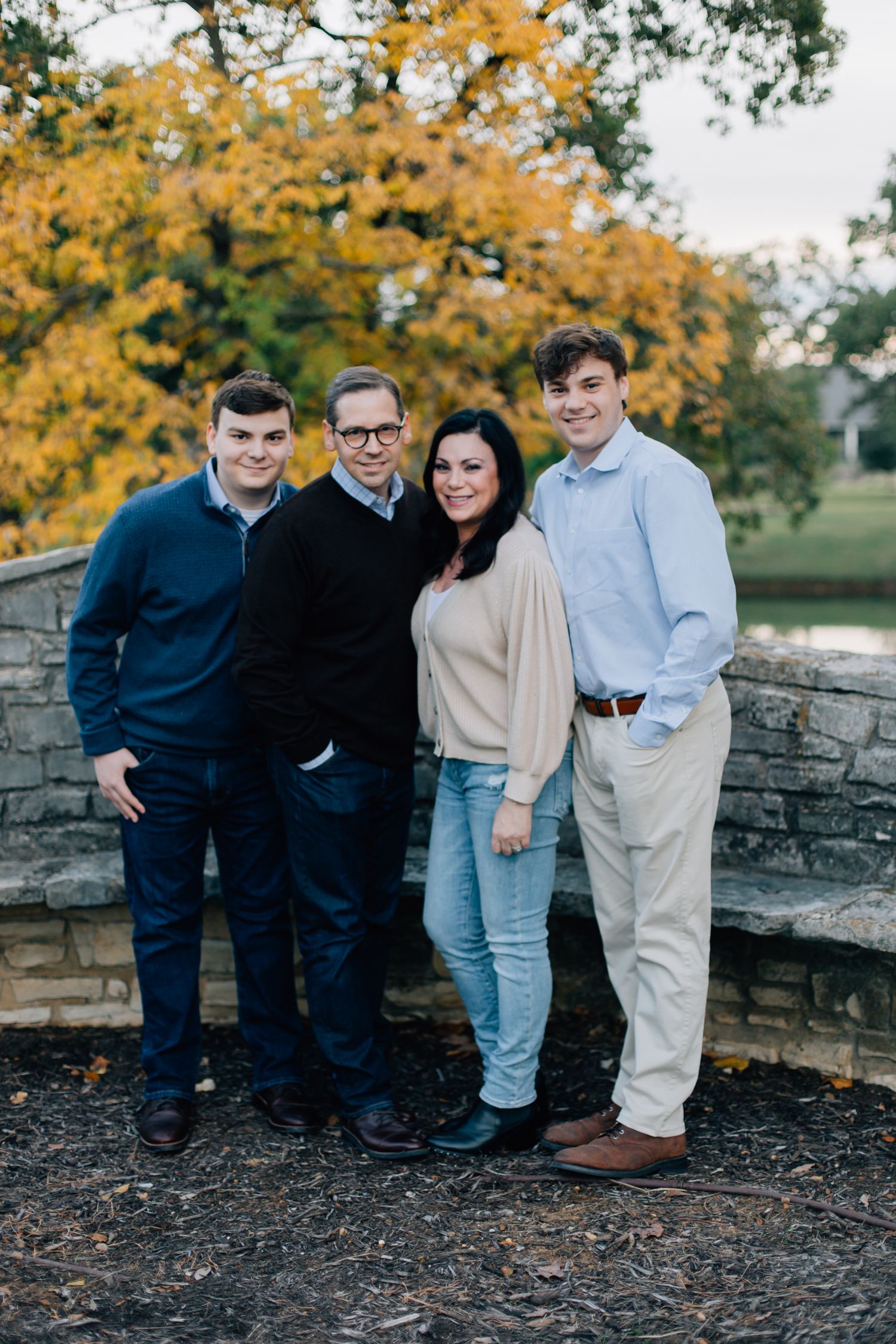 A group stands together against a stone wall with autumn foliage featuring bright yellow leaves in the background.