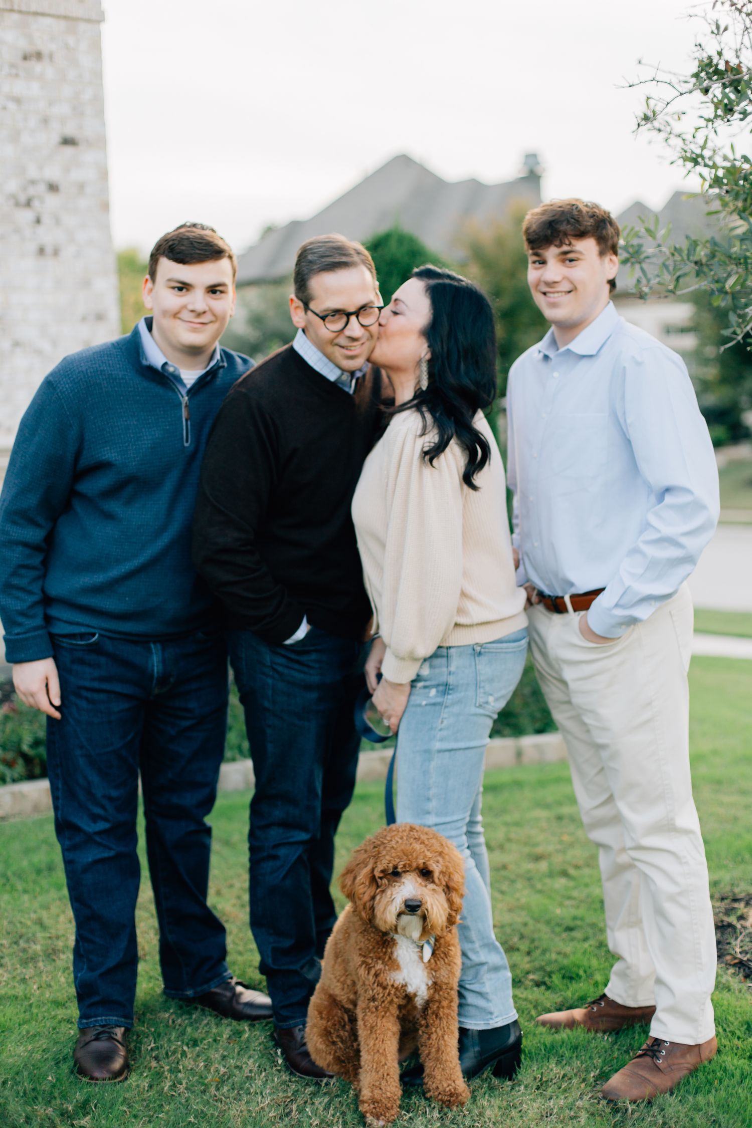 A group stands together outdoors with their goldendoodle dog during a casual portrait session.
